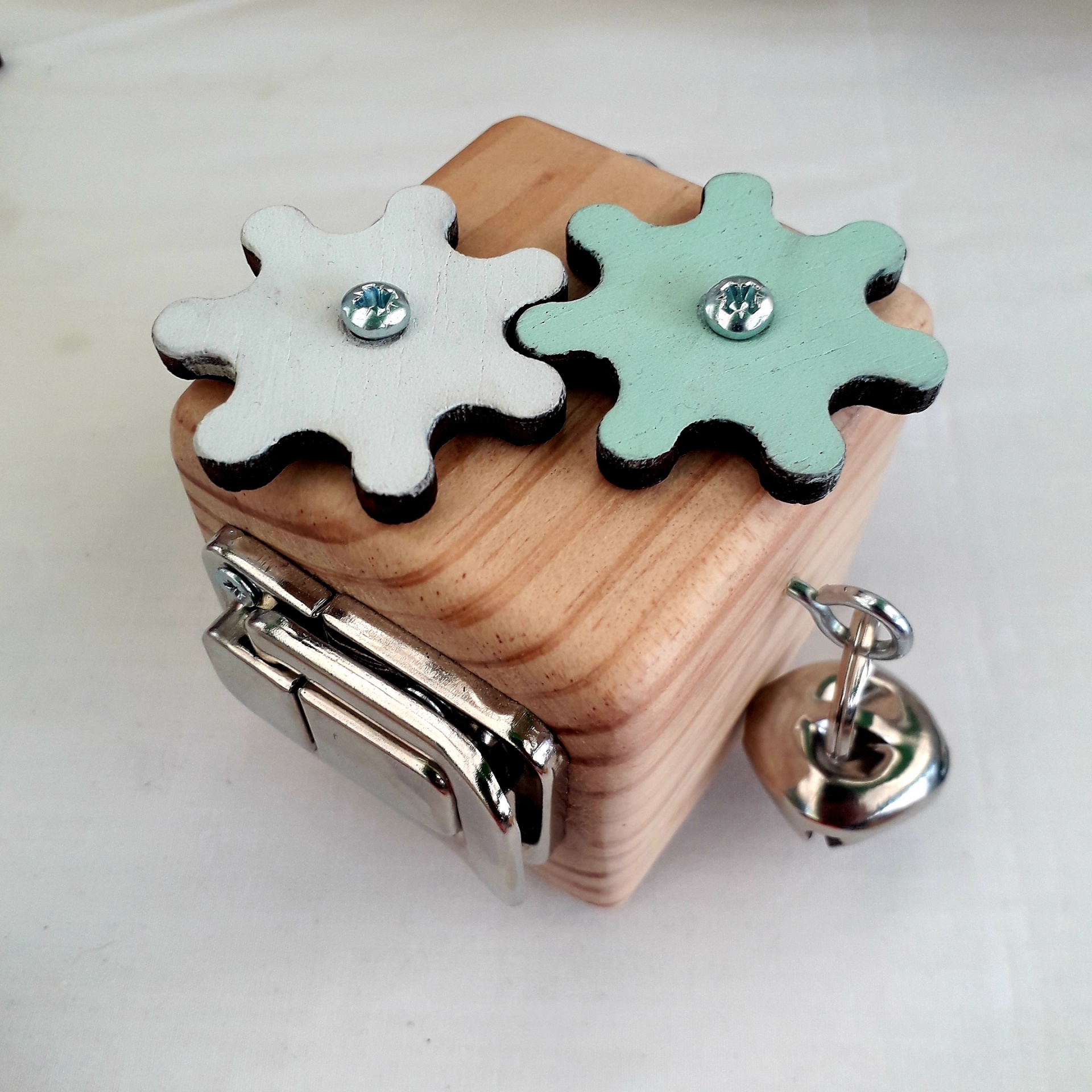 Cubo de Ação Caixa de madeira clara com duas engrenagens coloridas e uma campainha metálica.