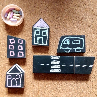 Blocos de giz com desenhos de casas, carrinha e estrada em cortiça com copo de giz colorido