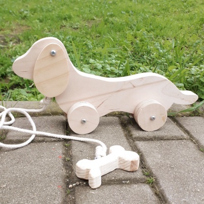 Brinquedo de cão em madeira com rodas e corda para puxar sobre pavimento com relva ao fundo