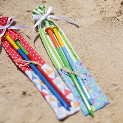 Dois pares de pauzinhos coloridos em bolsas de tecido listrado e geométrico na areia