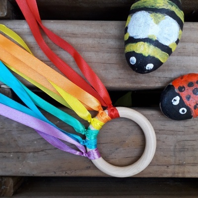 Argola de madeira com fitas coloridas e pedras pintadas de abelha e joaninha sobre madeira