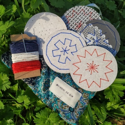 Discos de tecido bordados, caixa com linhas coloridas, etiqueta e tecido paisley sobre folhas verdes