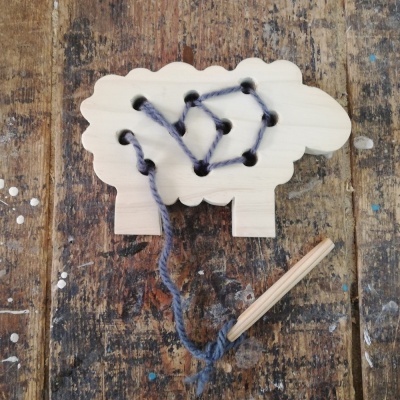 Jogo educativo de madeira em forma de ovelha com fio de lã azul escuro e lápis sobre madeira rústica