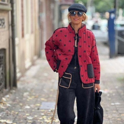 Mulher vestindo casaco vermelho com corações pretos e calças pretas passeio na cidade com cão