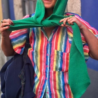 Mulher com camisa colorida e cachecol verde amarrado na cabeça em ambiente urbano