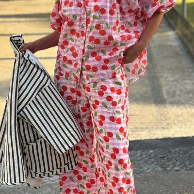 Pessoa vestindo conjunto de pijama com padrão de cerejas em fundo xadrez rosa, segurando casaco às riscas pretas e brancas ao ar livre
