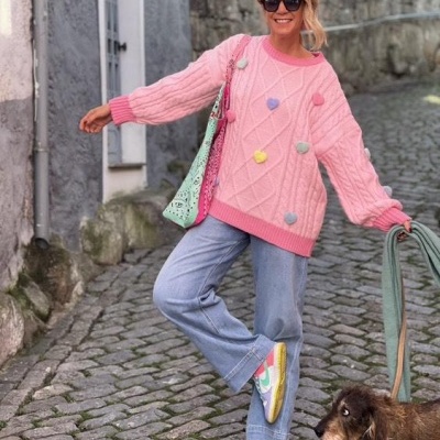 Mulher com camisola rosa de malha, calças de ganga e sapatilhas coloridas, segurando a trela de um cão na rua de calçada portuguesa
