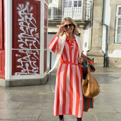 Mulher com vestido listrado vermelho e branco, óculos de sol e botas castanhas num cenário urbano