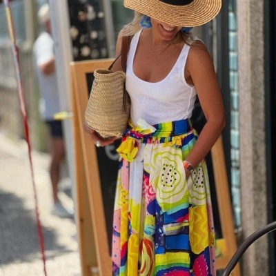 Mulher com vestido longo colorido, chapéu de palha e bolsa de palha