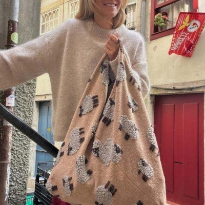 Mulher segurando bolsa bege com padrão de ovelhas em ambiente urbano