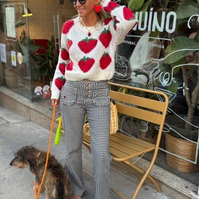 Mulher com camisola de morangos e calças xadrez em frente a café com cão.