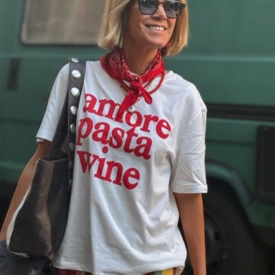 Mulher de cabelo loiro curto com t-shirt branca com texto vermelho e lenço vermelho ao pescoço