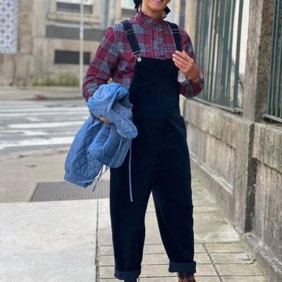 Mulher com jardineira preta, camisa xadrez, óculos de sol, sapatos castanhos e jaqueta azul clara