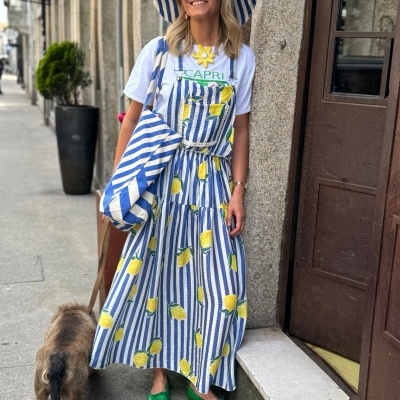 Mulher com vestido e chapéu às riscas azuis e brancas com limões, T-shirt branca 'CAPRI', sapatos verdes e bolsa grande, em passeio na cidade.