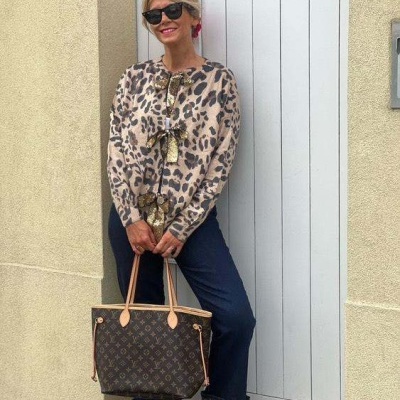 Mulher com blusa de padrão animal print, calças azuis viradas, sapatos vermelhos e mala Louis Vuitton.