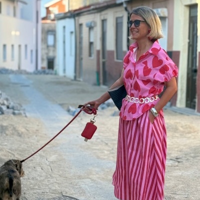 Mulher com roupa rosa e vermelha a passear com cão numa rua urbana