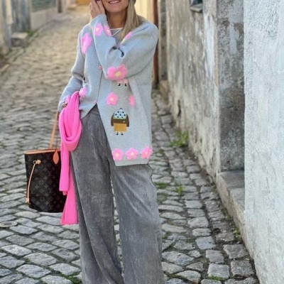 Mulher com casaco cinza de flores rosas, calças cinzentas largas e sapatos amarelos numa rua de calçada portuguesa