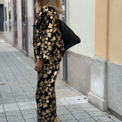 Mulher com conjunto floral dourado e preto numa rua de pedra clara