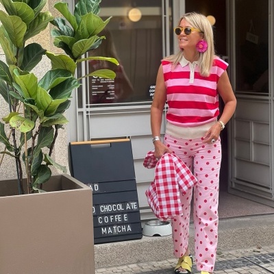Mulher vestindo roupa colorida com padrões às riscas e bolinhas, em frente à loja com placa preta com letras em branco.