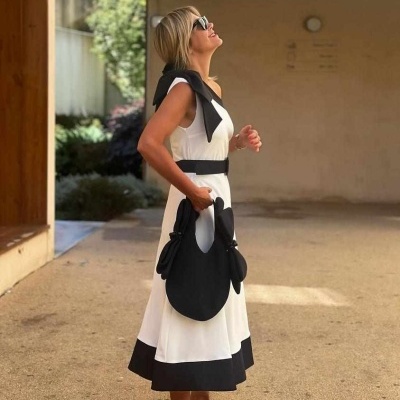 Mulher com vestido branco e detalhes a preto segurando mala preta e usando chinelos