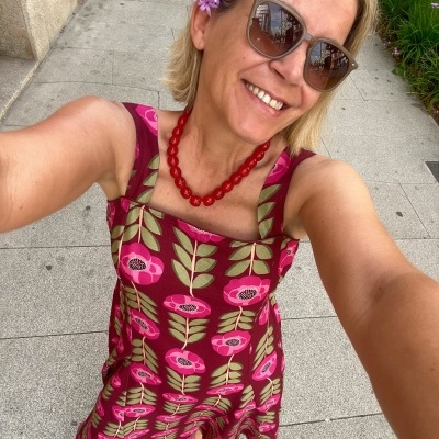 Mulher com vestido floral vinho, colar vermelho, óculos de sol e sapatilhas rosas num passeio urbano