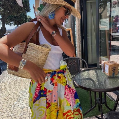 Mulher com vestido colorido e chapéu de palha sentada numa esplanada