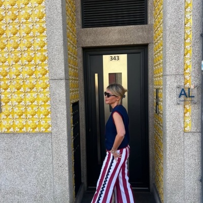 Pessoa com calças de riscas vermelhas e brancas e colete azul junto a porta número 343 com azulejos amarelos na parede