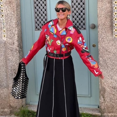 Mulher com casaco vermelho estampado e saia preta frente a porta azul