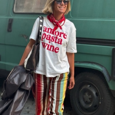 Mulher com t-shirt branca com texto vermelho, calças às riscas coloridas e lenço vermelho no pescoço