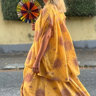 Mulher com vestido amarelo estampado de girassóis e leque colorido numa rua