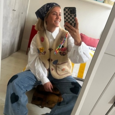 Mulher tirando selfie no espelho com colete peludo, lenço na cabeça e jeans com corações pretos