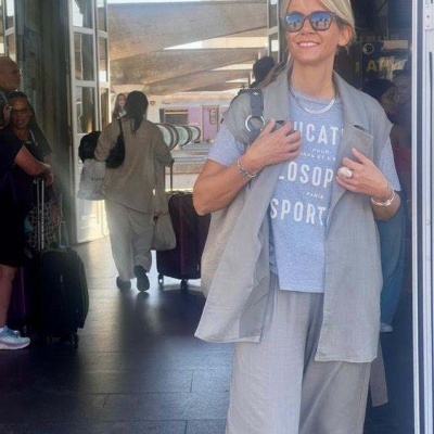 Mulher com fato cinza e t-shirt azul claro com texto branco numa estação de comboios