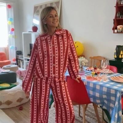 Mulher vestindo pijama listrado vermelho e rosa com corações no interior de uma sala com mesa posta.