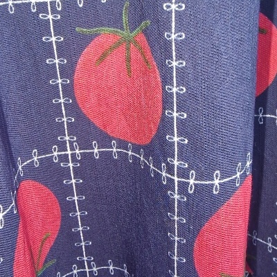 Tecido azul com padrão de tomates vermelhos e linhas brancas formando uma grade.