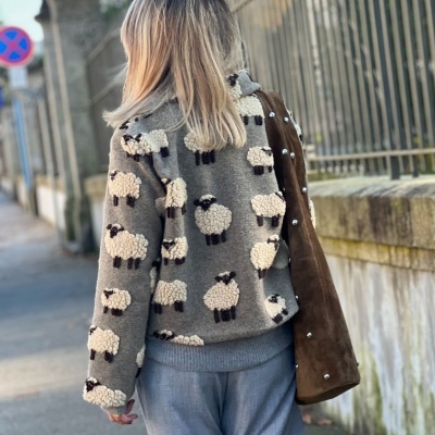 Casaco cinza com padrão de ovelhas e bolsa castanha em ambiente urbano