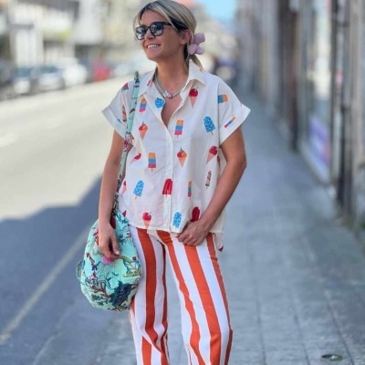Mulher com camisa estampada de gelados e calças laranja às riscas na rua
