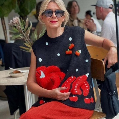 Mulher sentada com colete preto estampado em vermelho e saia vermelha.