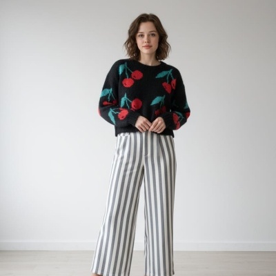 Mulher com camisola preta de cerejas vermelhas e calças riscas verticais brancas e cinzentas