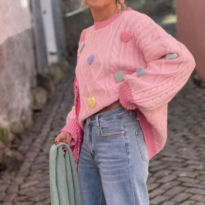 Camisola rosa de malha com pompons coloridos e jeans azul claro num ambiente urbano