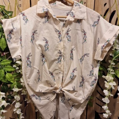 Camisa bege com padrão de coelhos pendurada num cabide de madeira