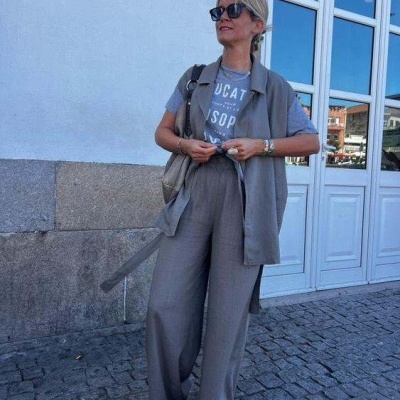 Mulher com roupa cinza e óculos de sol junto a parede e portas brancas