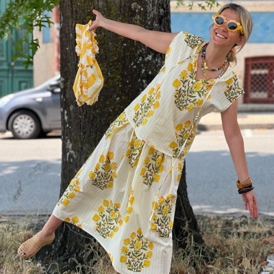 Mulher com conjunto branco e amarelo floral, bolsa amarela e óculos de sol amarelos em ambiente urbano