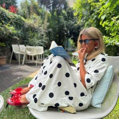 Mulher com vestido branco de bolinhas pretas sentada a ler livro num jardim