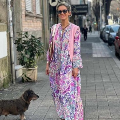 Mulher com vestido floral comprido e overlayer rosa a andar na rua com um cão
