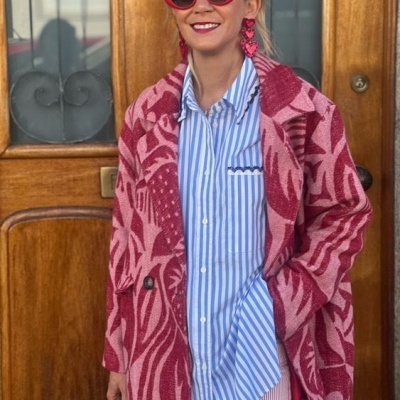 Mulher com casaco vermelho e rosa com padrão abstracto, óculos de sol vermelhos e brincos vermelhos