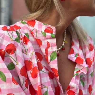 Blusa rosa com padrão de cerejas vermelhas e verdes e acessórios combinando