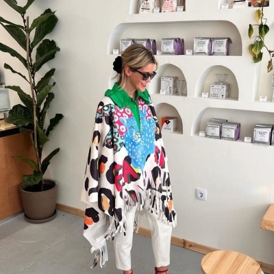 Mulher com poncho colorido em sala clara com prateleiras embutidas e plantas