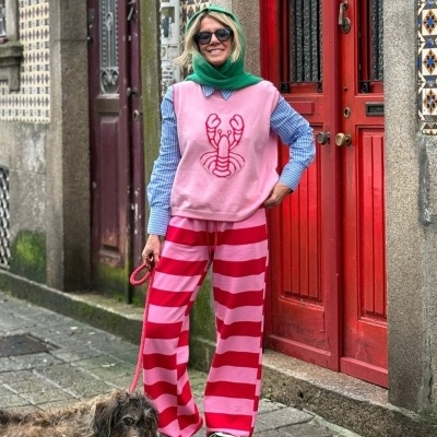 Pessoa com roupa colorida em frente a porta vermelha numerada 5 numa rua com calçada e azulejos tradicionais