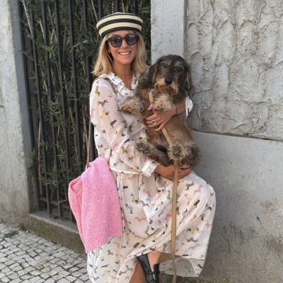 Mulher com vestido estampado a segurar cão castanho junto a parede de cimento