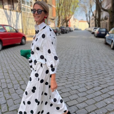 Vestido branco com bolinhas pretas em mulher a andar numa rua de calçada